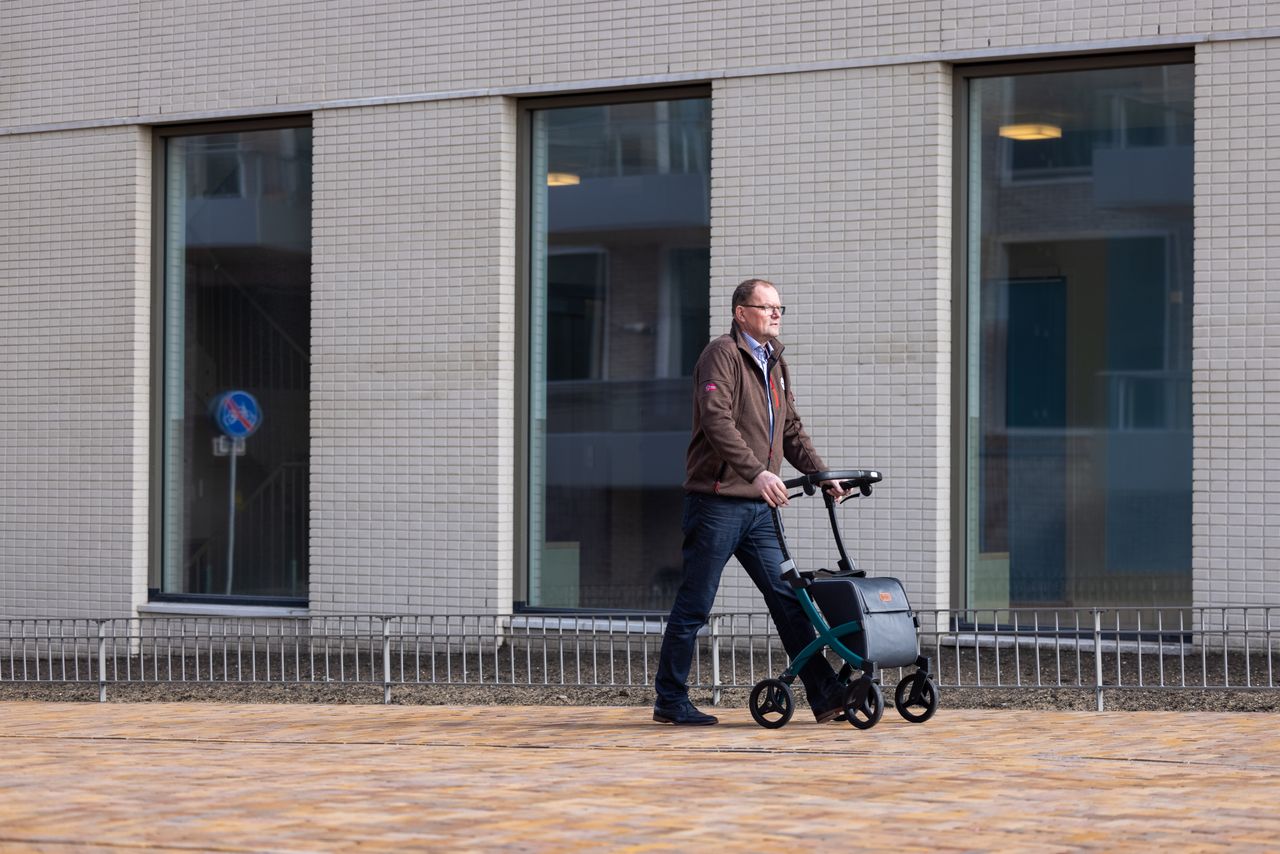 Senior man with rollator strolling outside city building on sunny day.