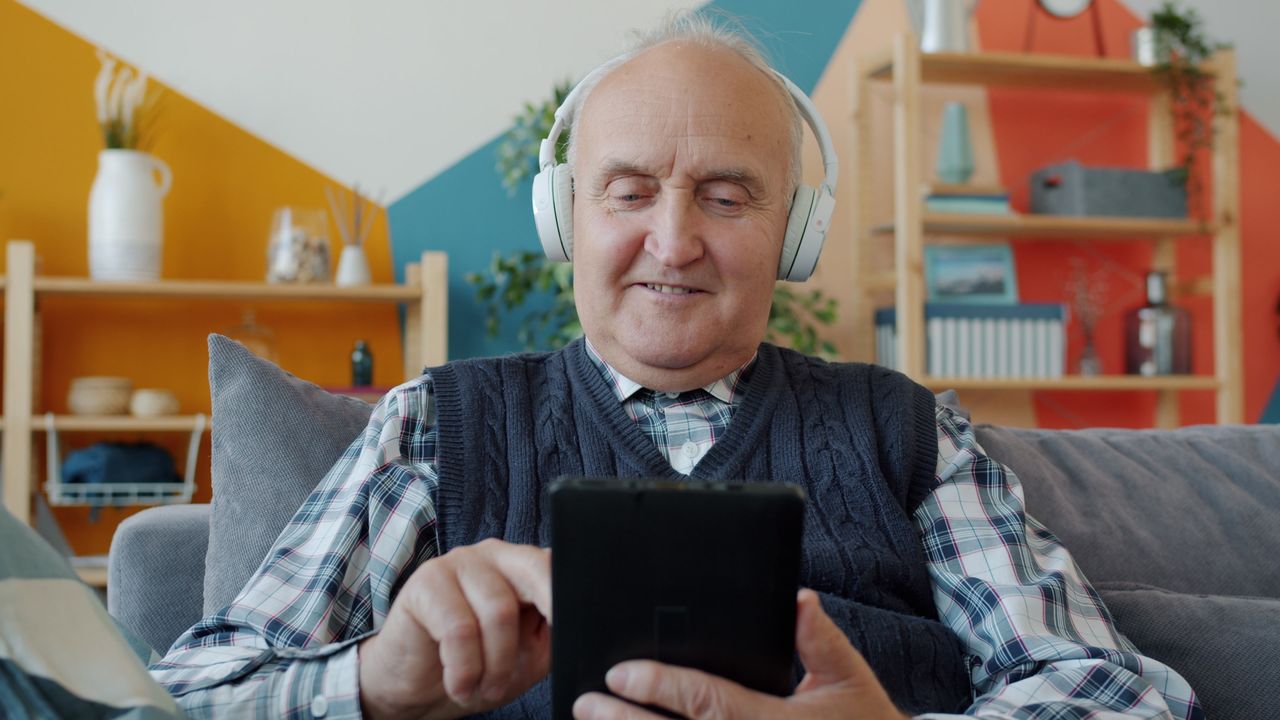 Elderly man using a tablet and headphones at home, relaxing leisure time.