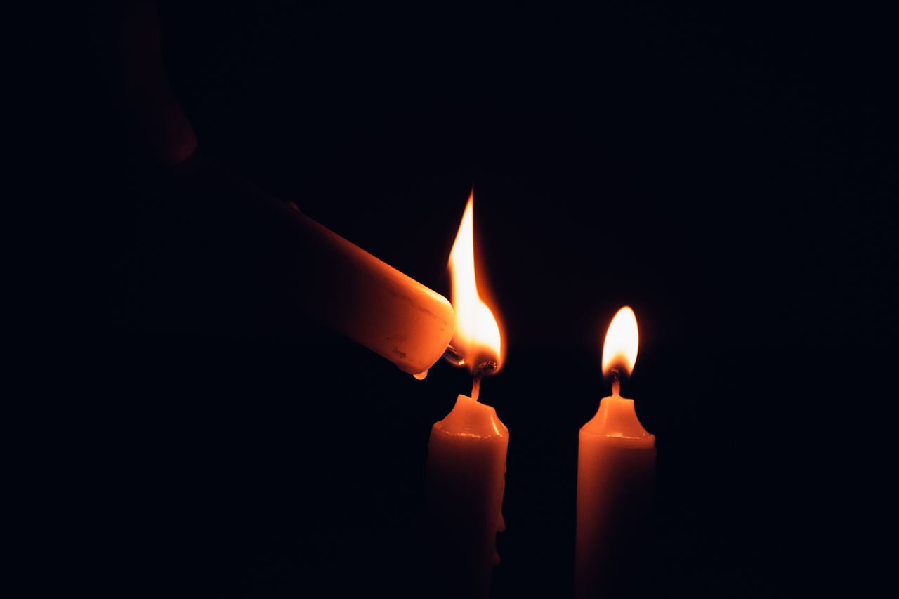 Two burning candles casting a warm glow in a dark setting, symbolizing warmth and solitude.