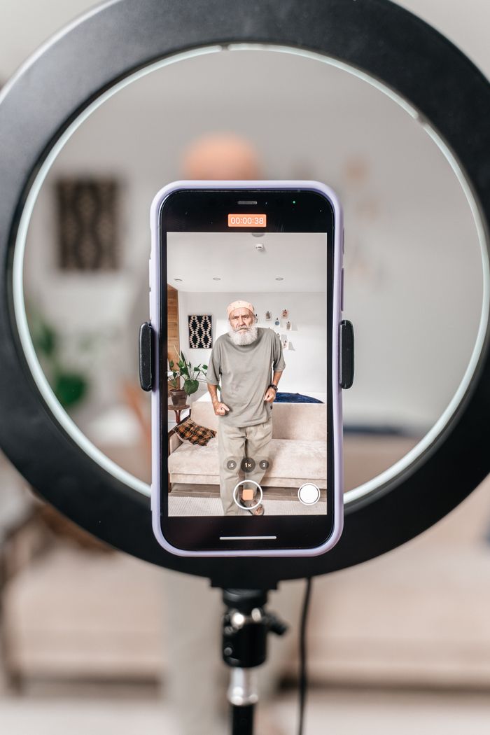 Elderly man using a smartphone with a ring light to record a video at home.